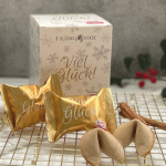 1 Faltschachtel für 8 Glückskekse mit einem Viel Glück-Motiv, 2 Glückskekse in einer goldenen Viel Glück Verpackung, 2 separate Glückskekse und eine Vanille-Schote